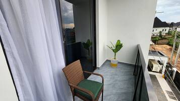 A balcony with a wicker chair, a potted plant, and a view of the surrounding area.