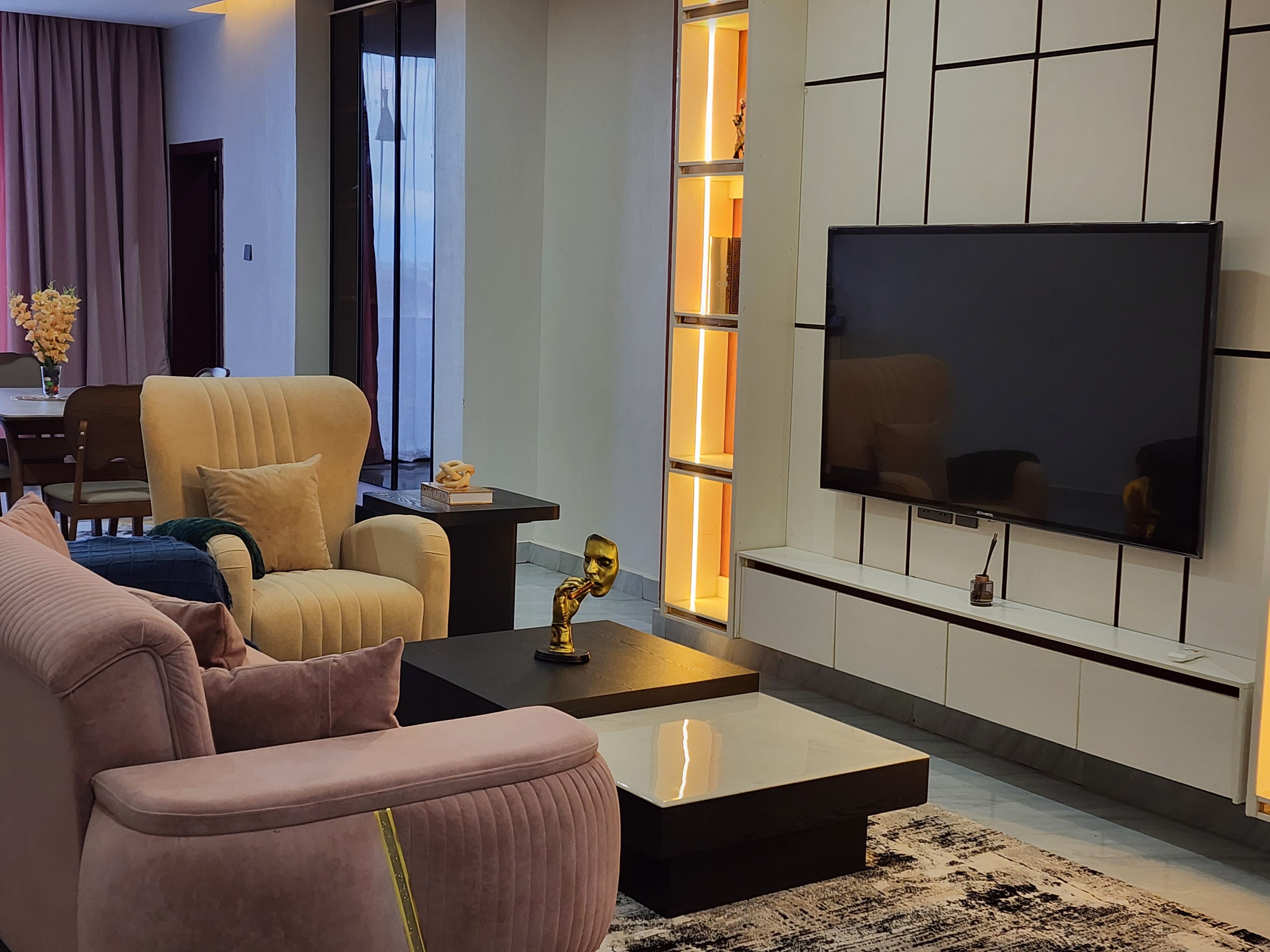 A modern living room with a sofa, armchair, coffee table, and a flat-screen TV mounted on the wall.