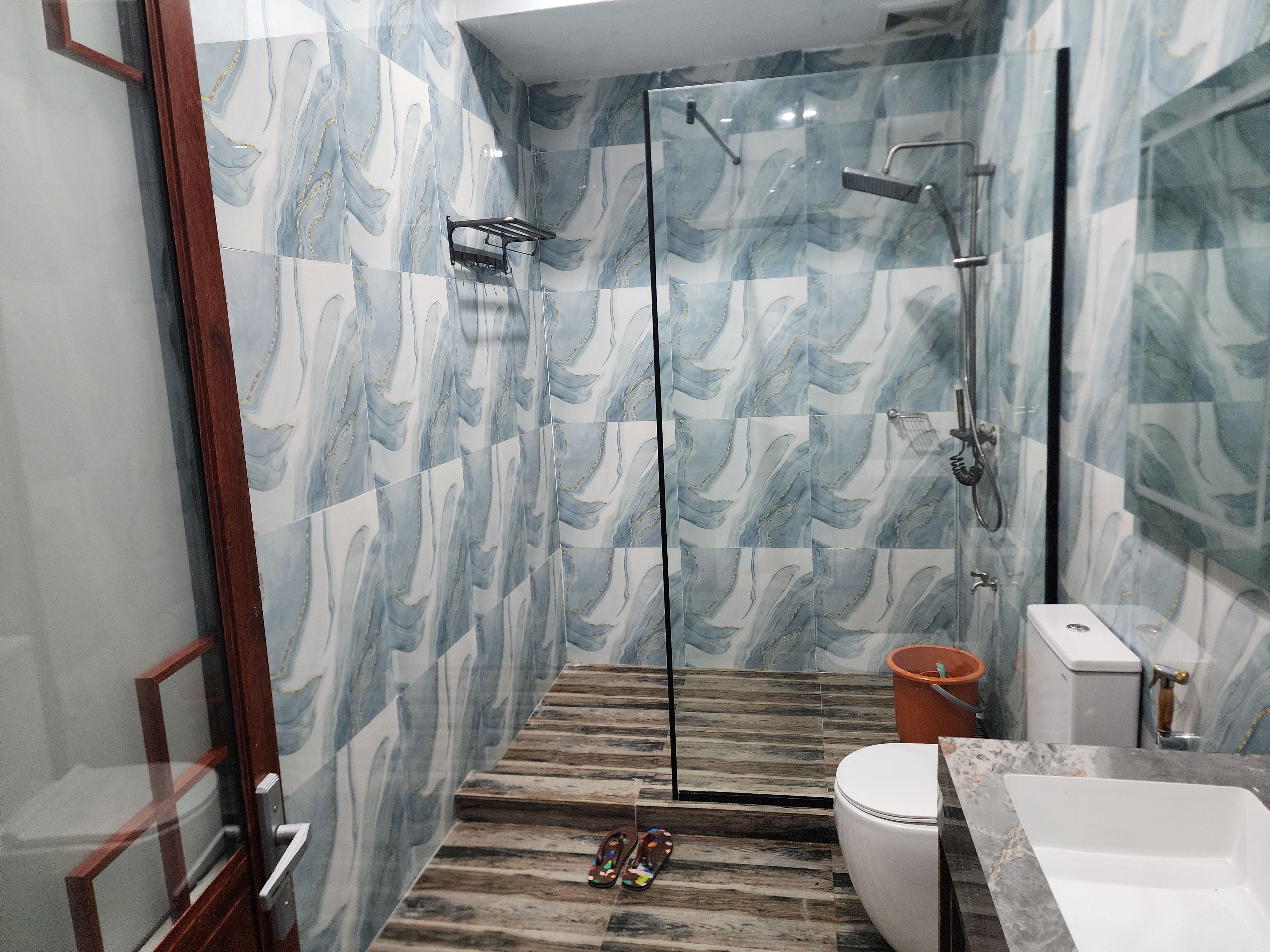 Un baño con cabina de ducha de vidrio, suelo de madera, inodoro blanco y lavamanos de mármol.