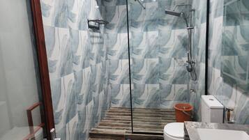 Un baño con cabina de ducha de vidrio, suelo de madera, inodoro blanco y lavamanos de mármol.