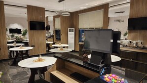 Interior moderno com mesas redondas, televisão de tela plana e recepção com uma tigela decorativa.