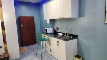 A compact kitchen with white cabinets, a black countertop, a green chair, and a small trash bin.
