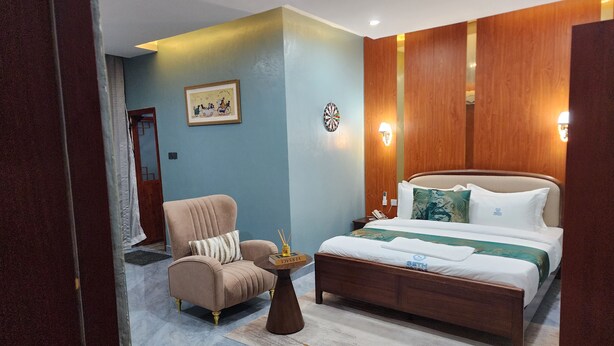 Een hotelkamer met een bed, een stoel, een nachtkastje en een wandlamp.