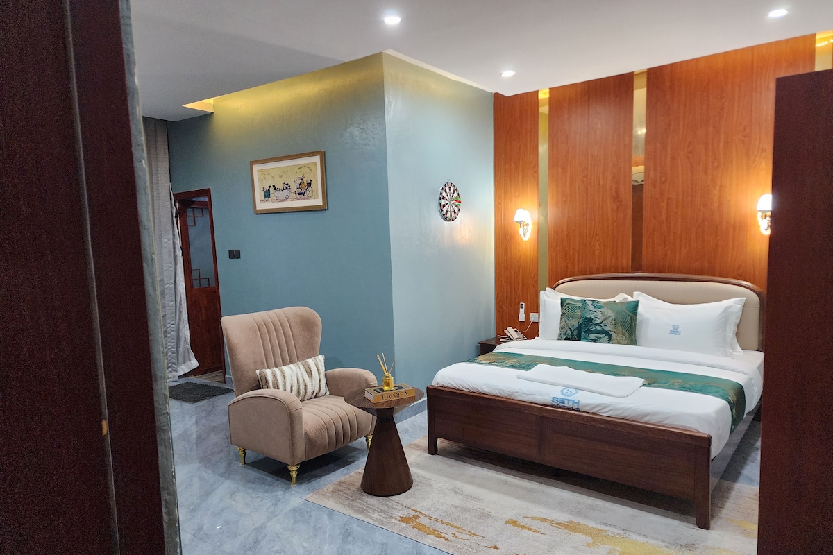 Una habitación de hotel con una cama, una silla, una mesita de noche y una lámpara de pared.