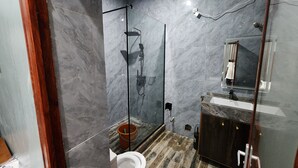 Casa de banho moderna com cabine de chuveiro de vidro, sanita e toucador com espelho.
