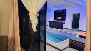 A modern indoor pool area with a reception desk, a seating area, and a glass partition.