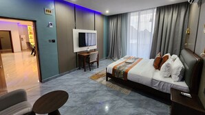 Quarto de hotel moderno com uma cama grande, televisão, escrivaninha e área de estar.