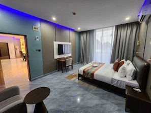 Habitación de hotel moderna con una cama grande, televisor, escritorio y zona de estar.