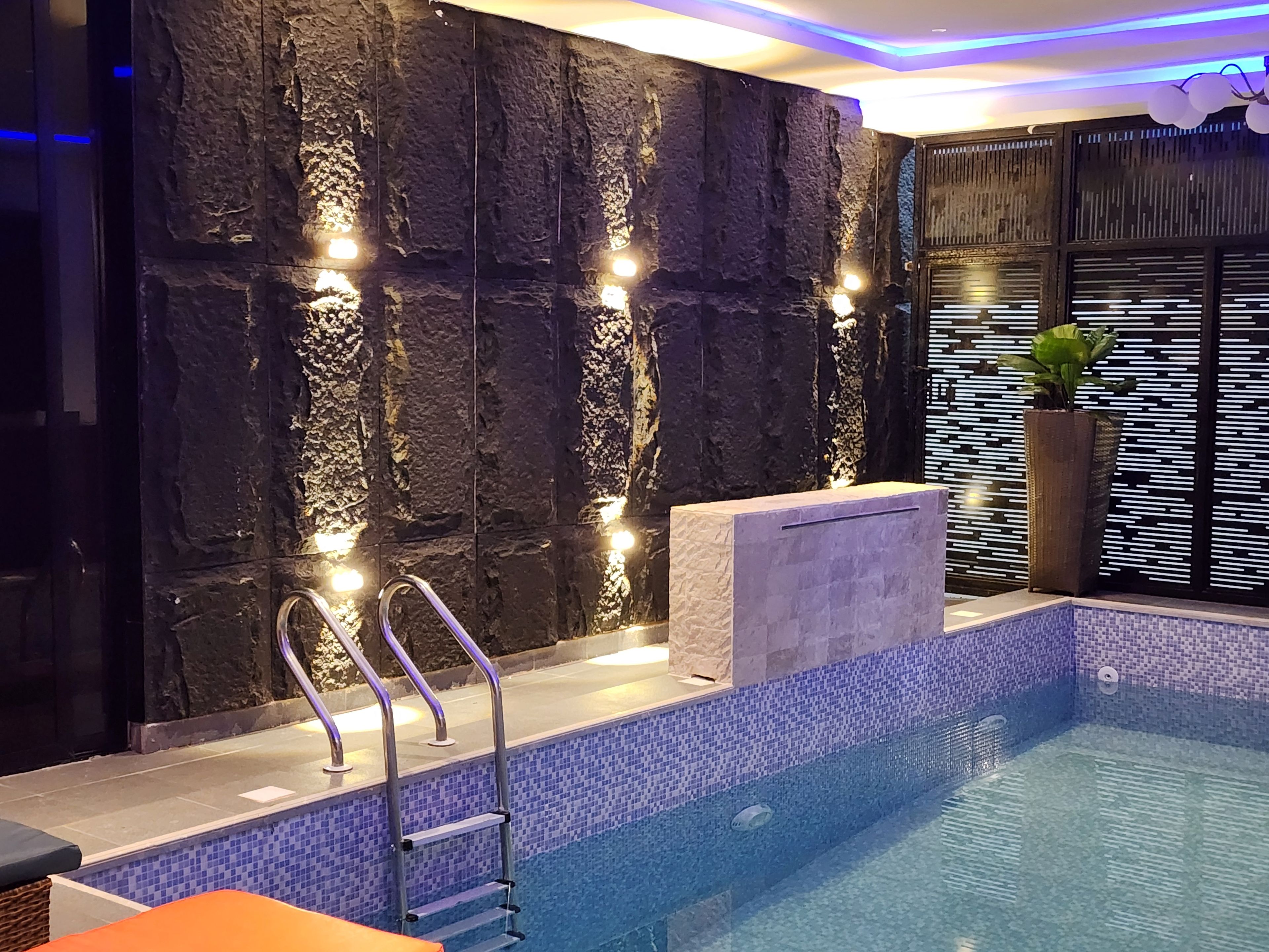 Un espace piscine intérieur moderne, avec un mur en pierre, un banc intégré et une échelle.