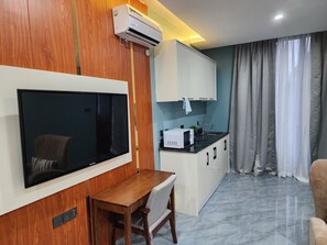A compact living space with a flat-screen TV mounted on a wooden wall, a small kitchen area with a microwave, and a dining table with a chair. - Sethhotel Apartment & Suite (Asaba)
