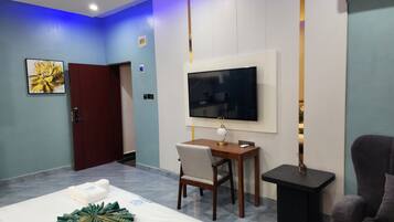 A hotel room with a bed, a desk with a chair, a television, and a sofa.