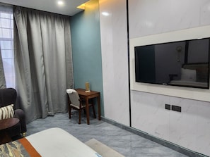 A hotel room with a bed, a desk, a chair, a television mounted on the wall, and a window with curtains.