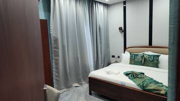 Ein Hotelzimmer mit Bett, Vorhängen, einem Nachttisch, einer Lampe und einem an der Wand befestigten Telefon.