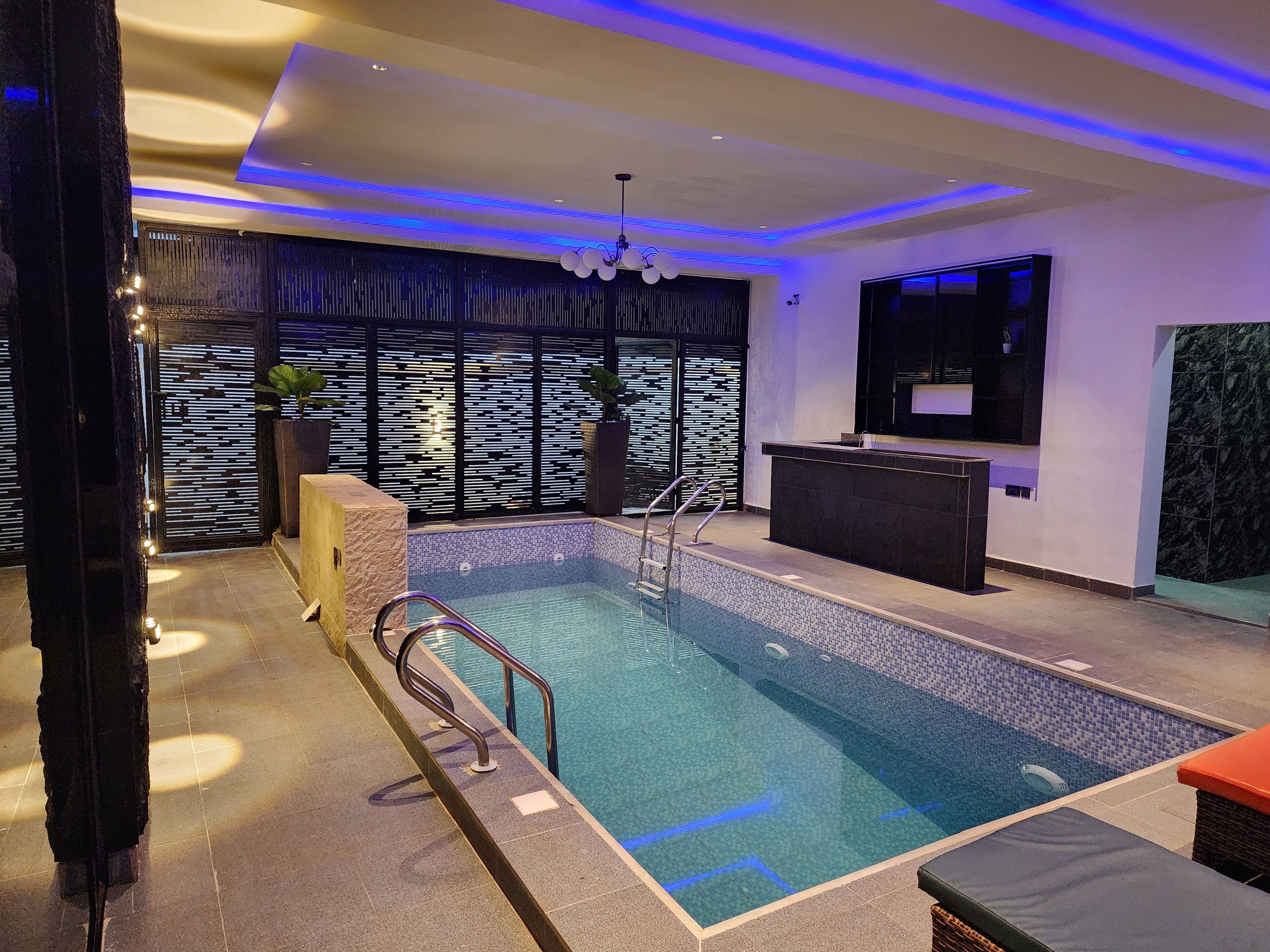 Una piscina interior moderna con borde de azulejos, un mostrador de recepción y una pared decorativa con líneas verticales.