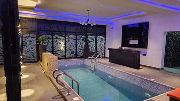 Una piscina interior moderna con borde de azulejos, un mostrador de recepción y una pared decorativa con líneas verticales.