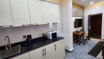 Una cocina moderna con armarios blancos, una encimera negra y un microondas. Hay una zona de comedor con una mesa y sillas, y un televisor montado en la pared.