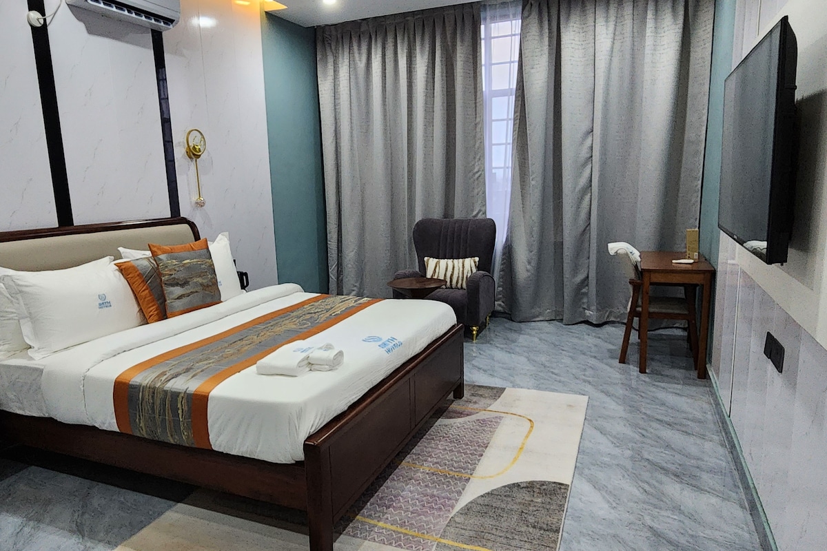 Habitación de hotel con cama, escritorio, silla, televisión y ventana con cortinas.