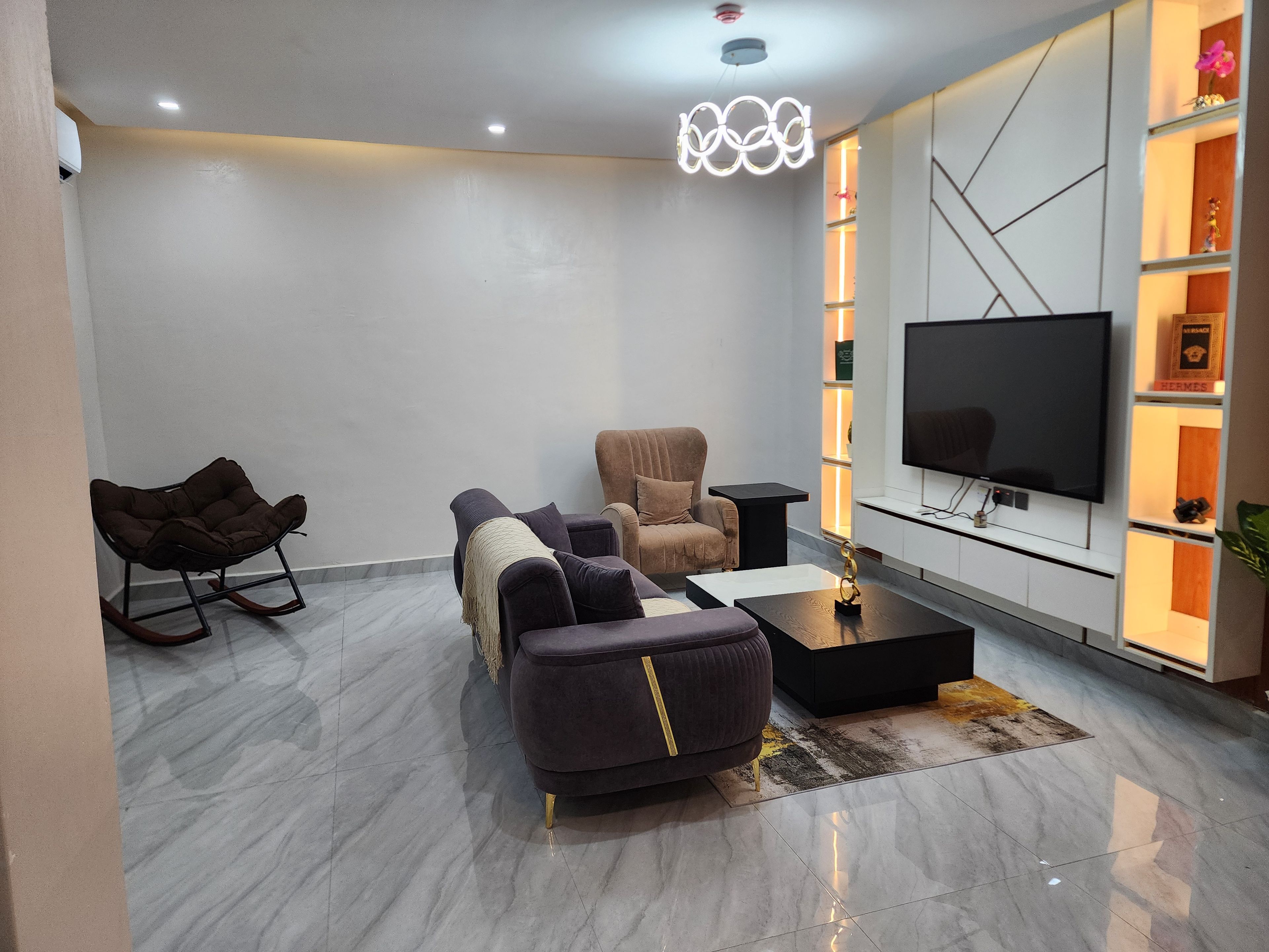 Ein modernes Wohnzimmer mit einer Couch, einem Sessel, einem Couchtisch und einem Flachbildfernseher.