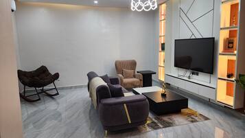 Ein modernes Wohnzimmer mit einer Couch, einem Sessel, einem Couchtisch und einem Flachbildfernseher.