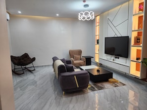 A modern living room with a sofa, armchair, coffee table, and a flat-screen TV.