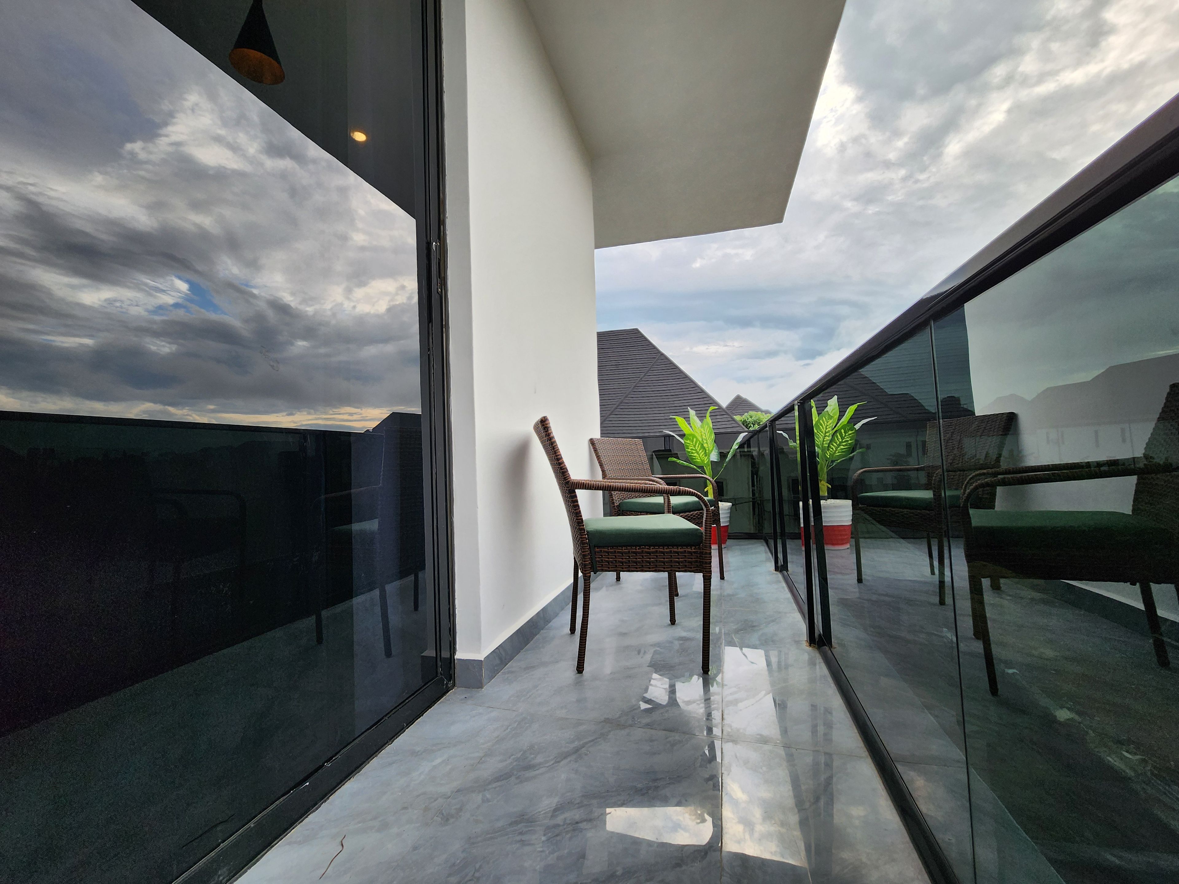 Ein Balkon mit Glasgeländer, Korbstühlen und Blumentöpfen.