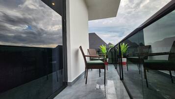 Ein Balkon mit Glasgeländer, Korbstühlen und Blumentöpfen.