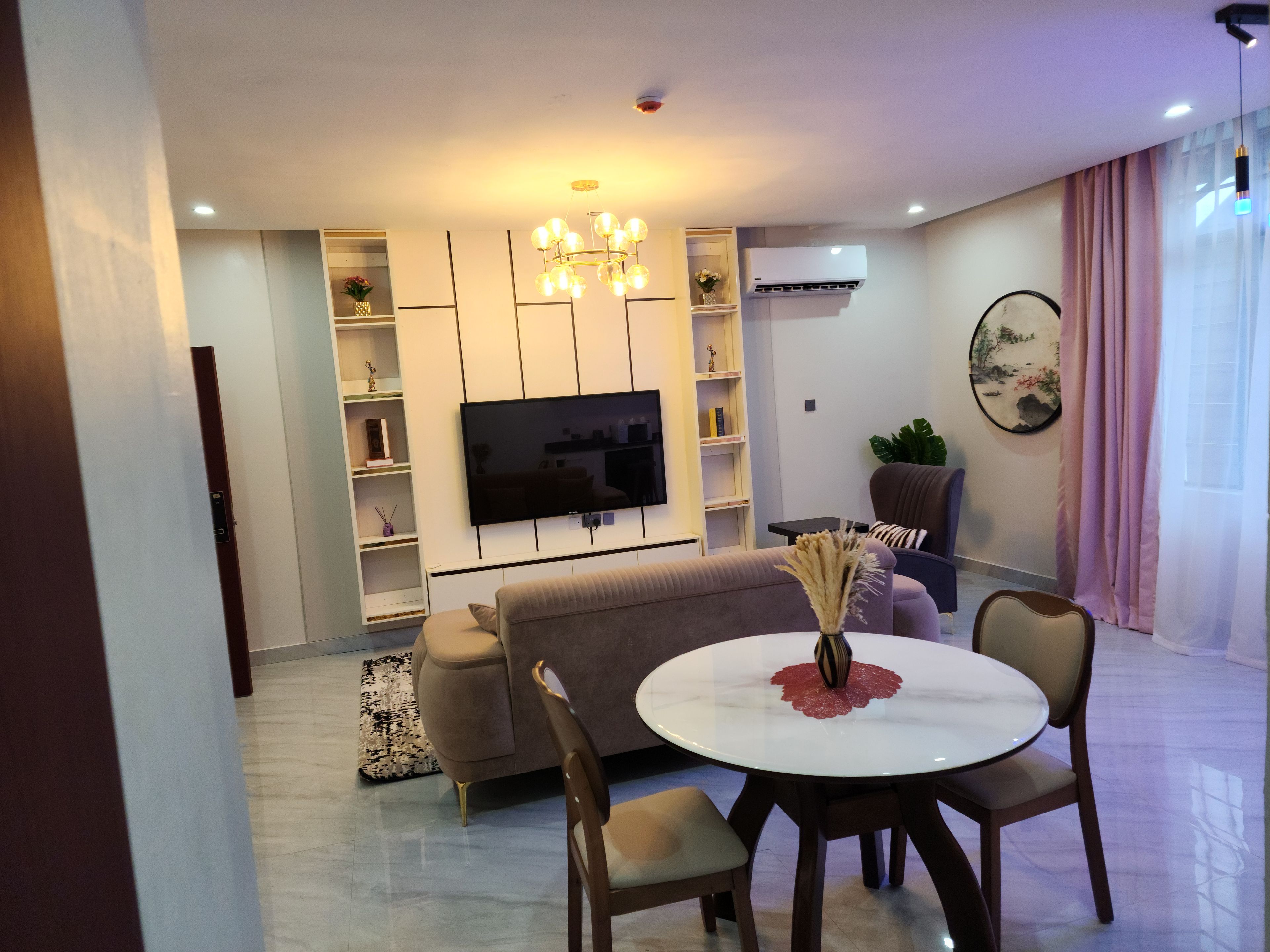 Un salon moderne comprenant un téléviseur à écran plat, un canapé, une table à manger avec des chaises et un vase décoratif.