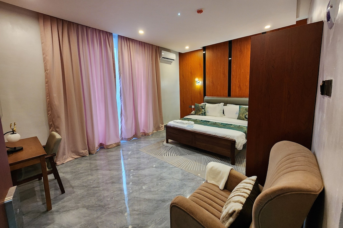 Habitación de hotel con cama, sofá, escritorio y ventana con cortinas.