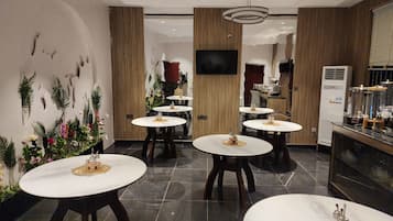 A modern interior with round tables, a flat-screen TV, and a kitchen area with a coffee machine.