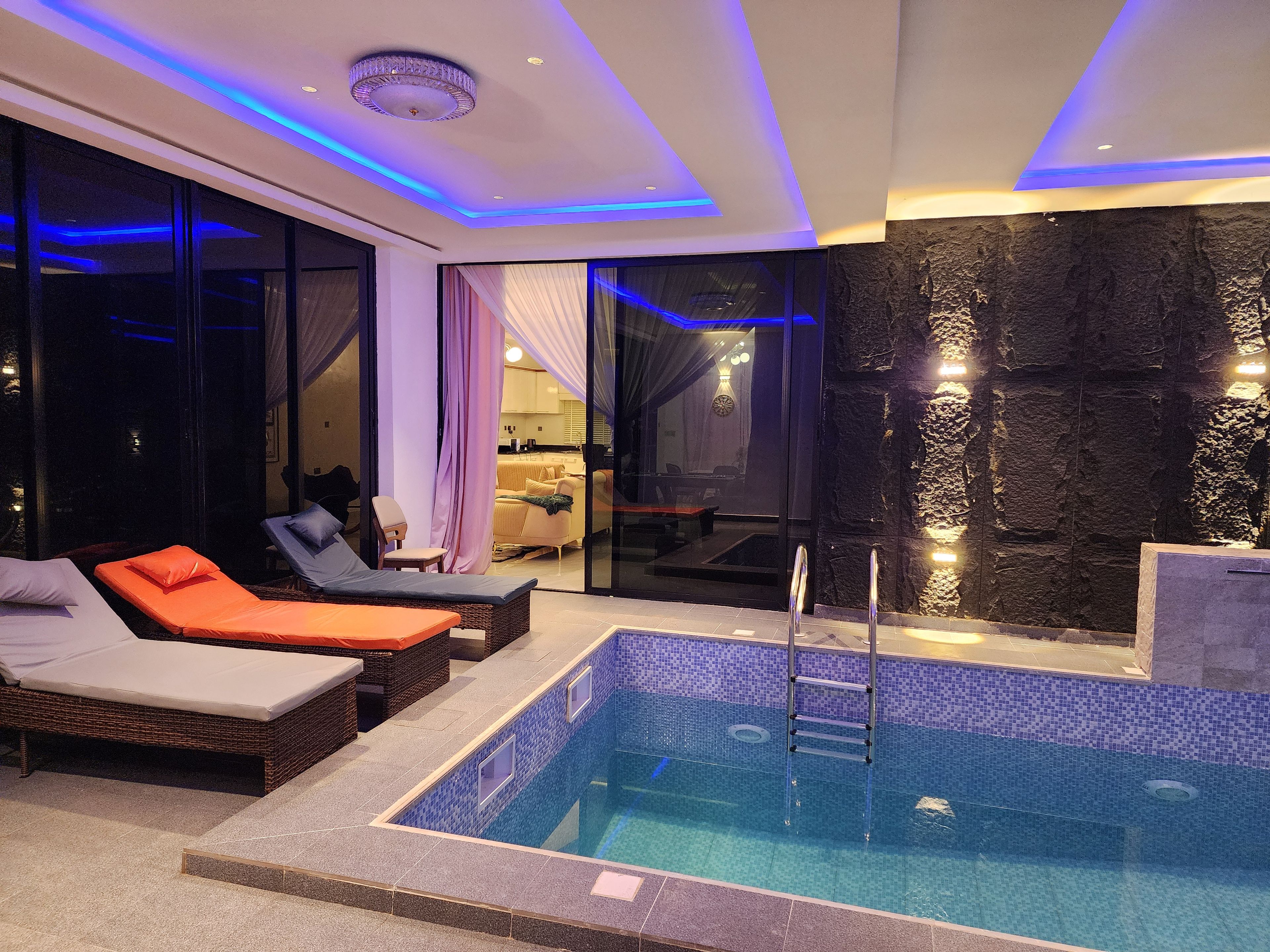 Un área de piscina interior moderna con sillones de descanso, una piscina pequeña y una pared de piedra.