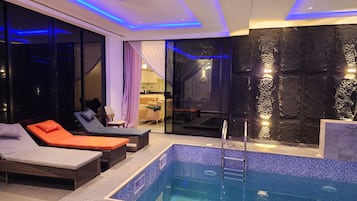 Un área de piscina interior moderna con sillones de descanso, una piscina pequeña y una pared de piedra.