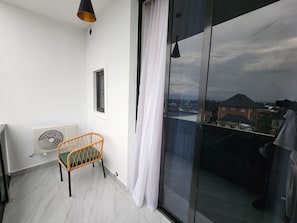 A balcony with a wicker chair, a white curtain, and a view of buildings.