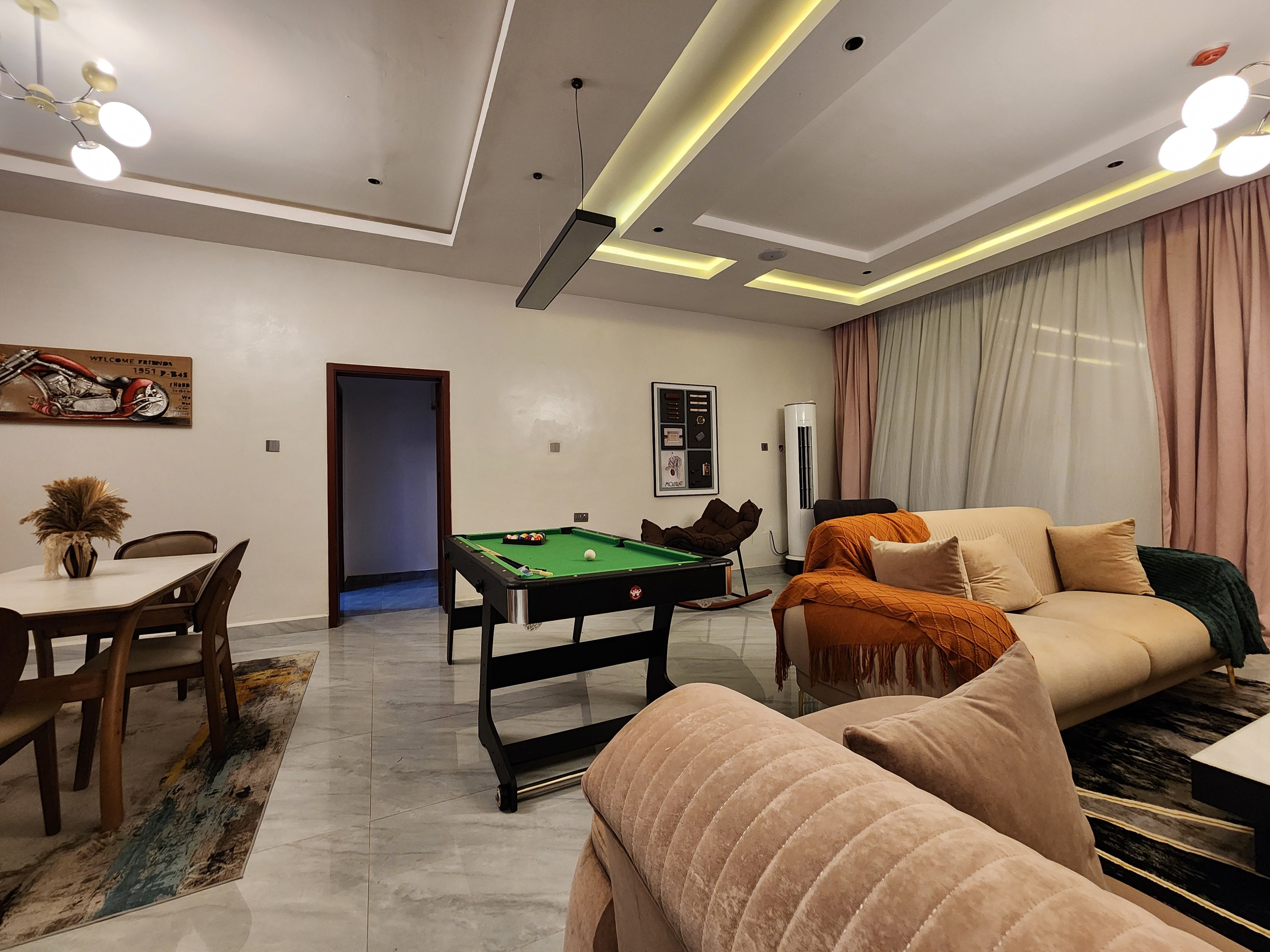 A modern living room with a pool table, a sofa, and a dining area with chairs and a table.