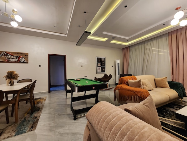 A modern living room with a pool table, a sofa, and a dining area with chairs and a table.