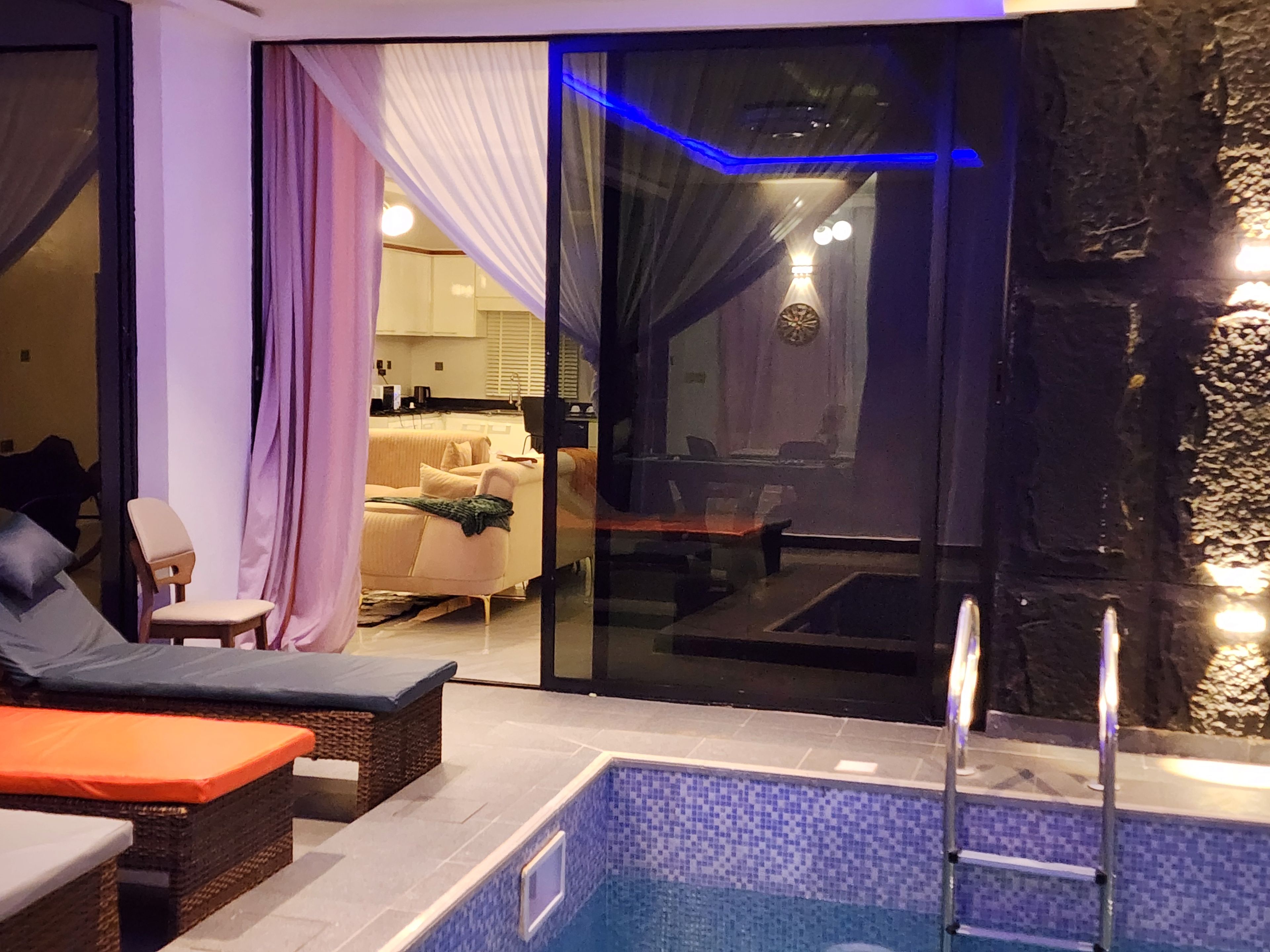 Zona de piscina con sillones de descanso, puerta de vidrio que da a una sala de estar y una pared de piedra.