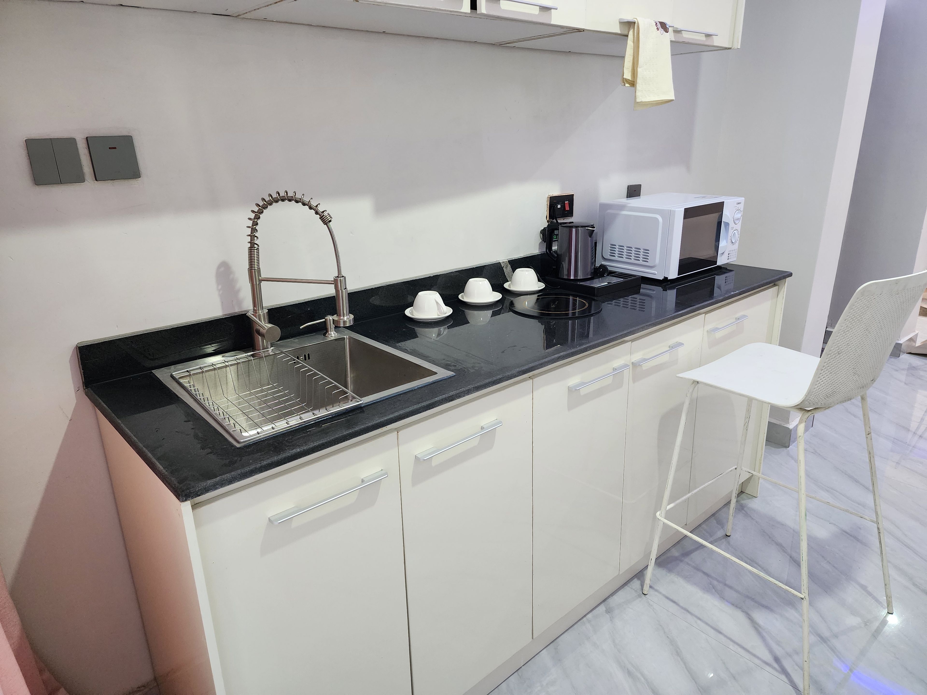A modern kitchen with a black countertop, stainless steel sink, white cabinets, a white chair, and a microwave.