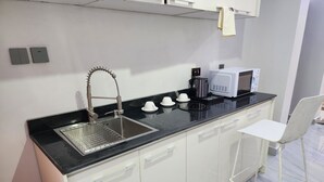 Een moderne keuken met een zwart aanrecht, een roestvrijstalen spoelbak, witte kastjes, een witte stoel en een magnetron.