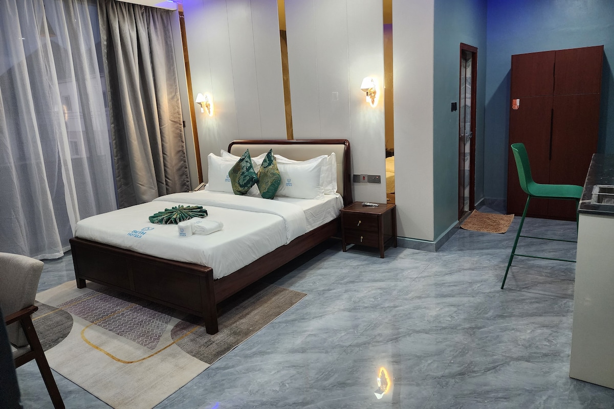Una habitación de hotel con cama, mesitas de noche, escritorio, silla y armario.