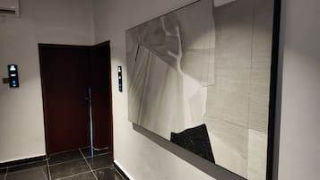 A hallway with a large abstract painting on the wall, a door, and a wall-mounted light switch.