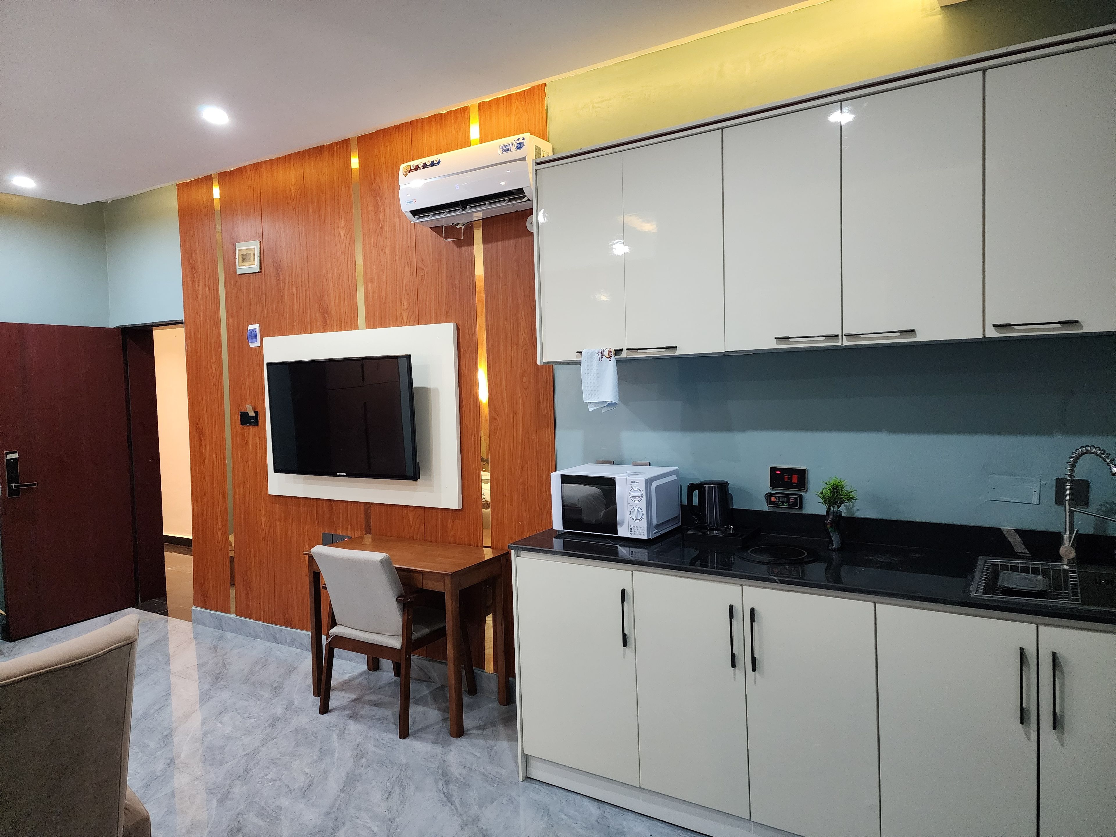 A modern kitchen with white cabinets, a built-in microwave, and a flat-screen TV.