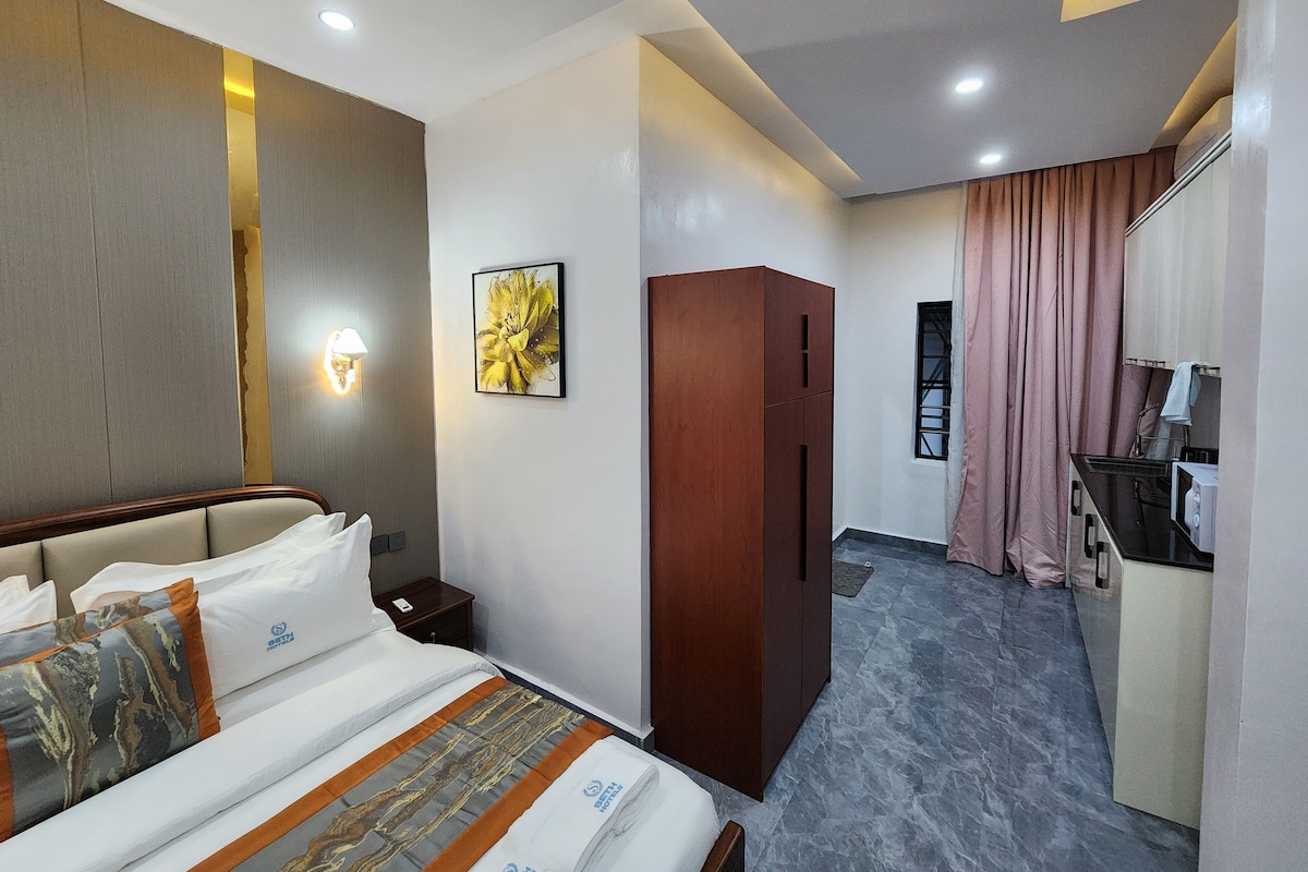 Habitación de hotel con cama, armario, escritorio con microondas y baño con ducha.