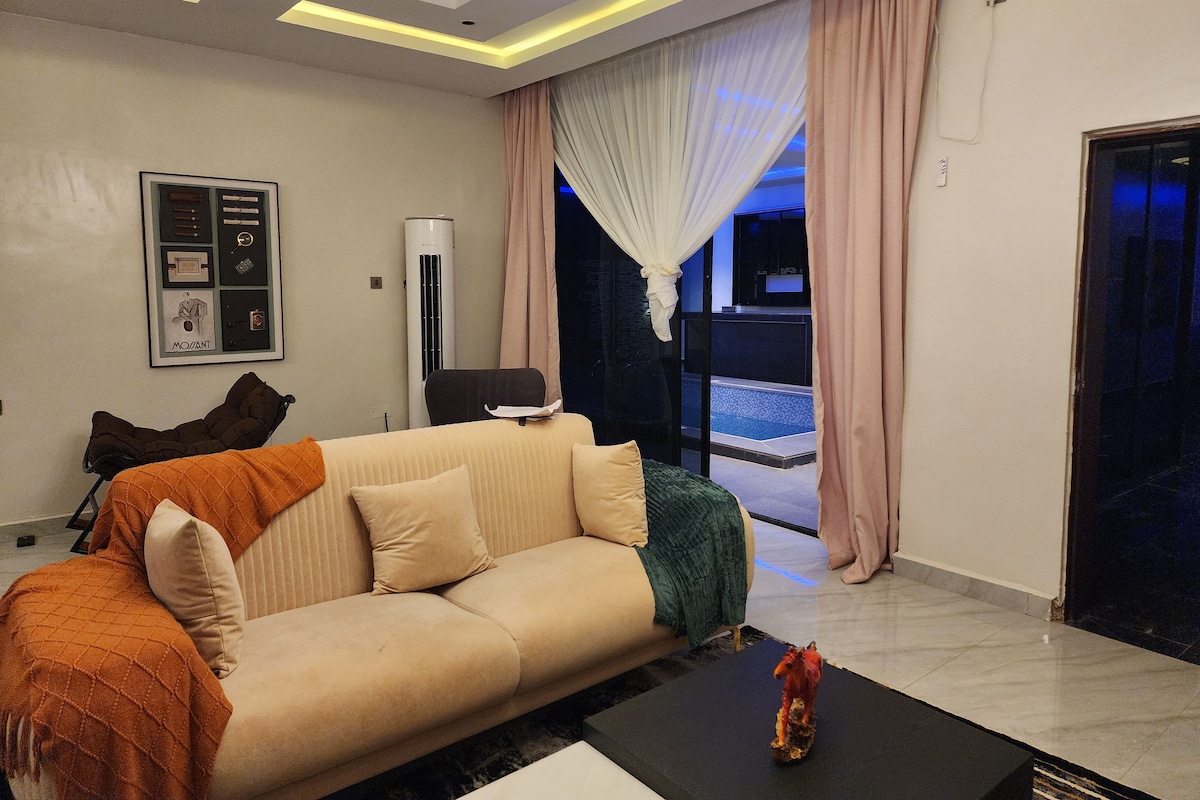 Una sala de estar moderna con un sofá, una mesa de centro y un objeto decorativo. Hay un ventanal con cortinas, un aire acondicionado instalado en la pared y un cuadro enmarcado.