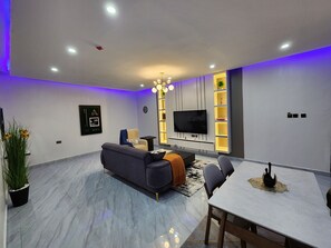 A modern living room with a sofa, a dining table, and a TV mounted on the wall.