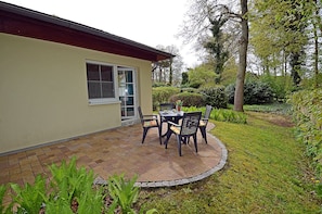 A patio with a table and chairs, a building with a window, and a garden with various plants. - First floor, central location, about 150 m from the sandy beach (Baltic Sea), accommodates up to 4 people (Juliusruh)
