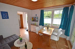 A cozy living room with a sofa, a dining table with chairs, a TV, and a window with curtains. - First floor, central location, about 150 m from the sandy beach (Baltic Sea), accommodates up to 4 people (Juliusruh)
