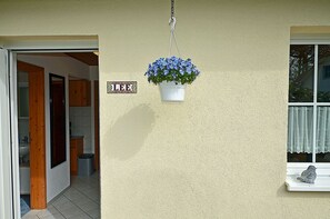 Ett hus med en hängande blomkruka på utsidan, ett fönster med en gardin och en liten fågelstatyett på fönsterbrädan.