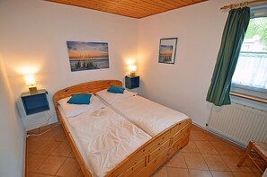 Ein Schlafzimmer mit einem hölzernen Bett, zwei Nachttischen mit Lampen, einem Fenster mit Vorhängen und zwei Wandbildern.