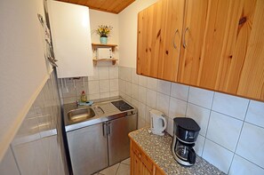 Ett kompakt kök med en dubbel diskho, en spis, en kaffebryggare och träskåp.