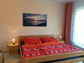A bedroom with a bed, two bedside tables, a night lamp, a painting, and a window with curtains. - Quiet location with a terrace, about 6 km from the Baltic Sea, about 800 m from the Bodden (Wiek)