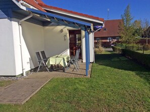 Ett takförsett utomhusområde med bord och stolar, en asfalterad gångväg och en byggnad med ett rött tak i bakgrunden.